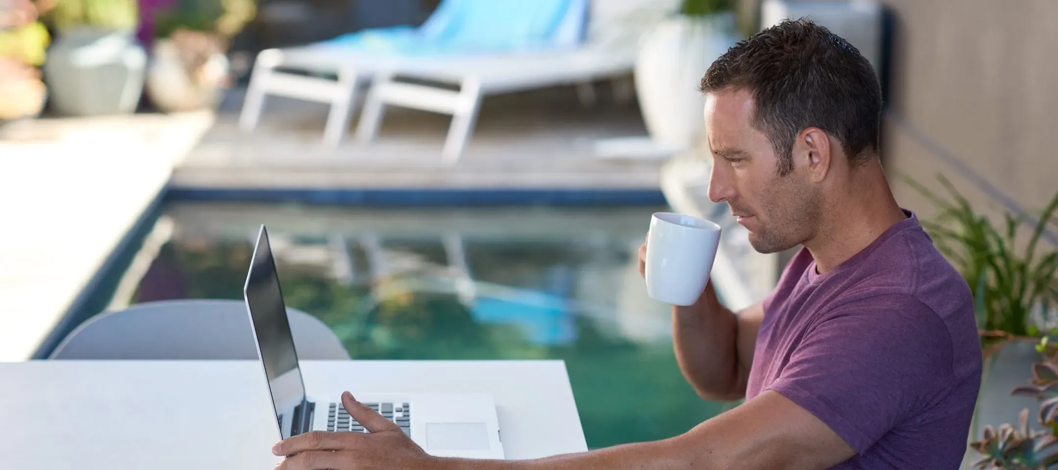 WTC Communications - Man working on laptop with coffee by pool in Kingston