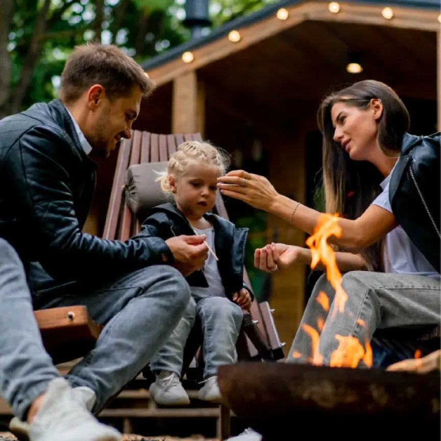 WTC Communications Gananoque - A family with a young child gathered around a campfire outside a cozy cabin connected to outdoor wi-fi WTC backyard beacon..
