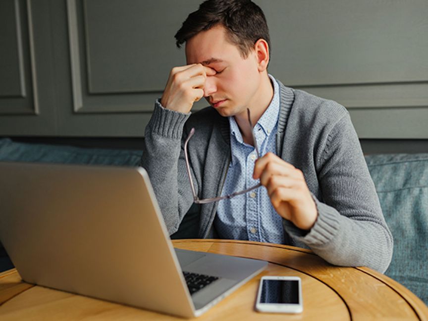 A person looks frustrated in front of a computer and phone