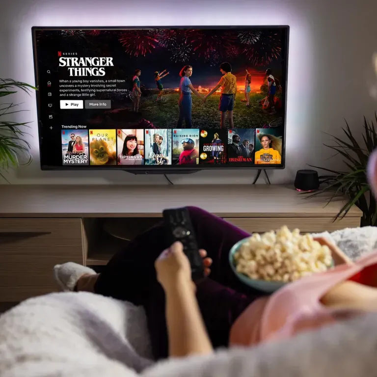 WTC Communications Kingston - Person relaxing on a coach watching Netflix on a TV with vibrant backlighting and enjoying popcorn.